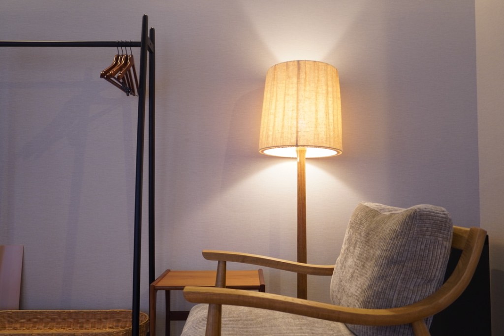 A cozy interior of a wellness space featuring a stylish floor lamp, a comfortable chair, a small wooden table, and a clothing rack with hangers.